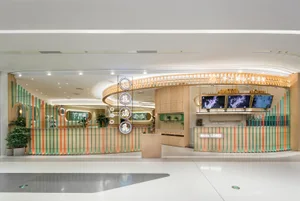 A warm and inviting hotel lobby with a wooden desk surrounded by potted plants and two TV screens on the wall