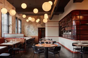 An inviting restaurant interior with wooden floors and walls, featuring dining tables and chairs, wine glasses, and bottles