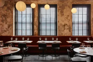 An inviting restaurant interior with wooden tables, chairs, and wine glasses, set up for a pleasant dining experience
