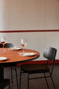 Empty dining area with a round wooden table, tile wall, and three wine glasses with red liquid