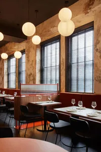 A warm and inviting restaurant interior with wooden tables, chairs, and wine glasses, featuring natural light from windows