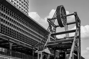 A building with a large metal structure in front of it, featuring many windows and a crane-like pulley system, suggesting a construction or renovation site