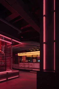 Office interior with two desks, chairs, and TV screens, surrounded by a red neon sign outside
