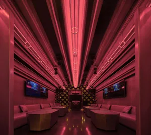 Modern living space with pink walls, ceiling lights, two couches, two chairs, and three TVs