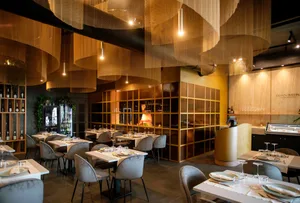 A cozy restaurant dining area with wooden tables, chairs, and wine glasses, set in a warm and inviting atmosphere