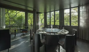 A dining area with a round table surrounded by chairs, wine glasses, and potted plants, creating a cozy atmosphere for gatherings and meals