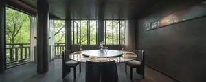 A dining area in a restaurant with a round table, wine glasses, and utensils, surrounded by large windows allowing natural light