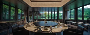 Dining area with a round table set with wine glasses, cups, bowls, and spoons, surrounded by chairs and two potted plants