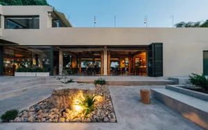 A cozy restaurant with a large stone wall and patio area, featuring dining tables, chairs, and potted plants
