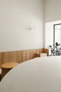 Clean and modern living area with a white wall, a window, a wooden table, and two potted plants, featuring simplicity and minimalism