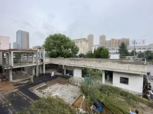 A busy construction site with a large concrete building under construction, featuring multiple floors, a rooftop area, and workers scattered throughout