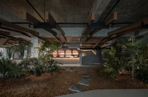 A modern dining space with concrete walls, wooden elements, and potted plants, featuring multiple tables and chairs
