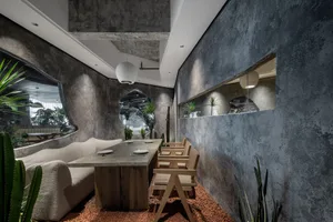 Cozy modern living space with a dining table, chairs, couch, and potted plant, surrounded by concrete walls and flooring