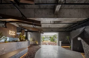 Open indoor space with a concrete floor, potted plants, and benches, featuring a doorway to another room and natural light
