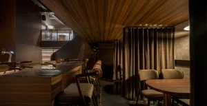 Cozy restaurant interior with wooden elements, black chairs, and a dining table, accompanied by a potted plant