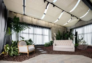 Cozy living area with a white couch, chairs, potted plants, and a bench, surrounded by natural elements