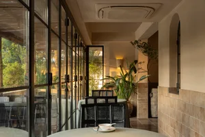 A modern restaurant interior with a dining area, tables, chairs, potted plants, and tiled walls creating a warm and inviting atmosphere