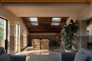 A warm and inviting living area with a dining table under a skylight, surrounded by chairs and a potted plant, with natural light filling the space