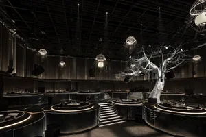 A modern event space with a tree sculpture on the stage, surrounded by tables and chairs, and multiple dining tables with chairs nearby