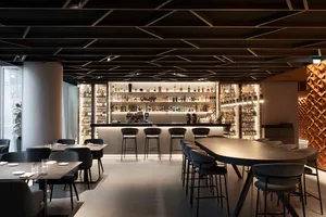 A modern bar area with a black and white color scheme, featuring a long counter and chairs, and a well-stocked counter with bottles