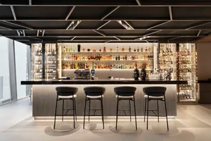 A modern bar with a long counter and four stools, featuring numerous bottles and a stylish design