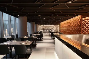 A modern restaurant interior with a long bar counter and dining tables, featuring sleek lines, contemporary elements, and warm inviting lighting