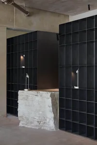 A dark and mysterious living space with a stone wall, a countertop, and a sink, lit by two lights on either side