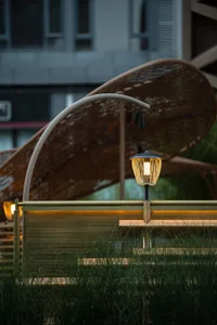A wooden bench under a large umbrella in front of a building, with two lights providing illumination and a relaxing atmosphere