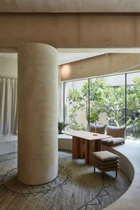 Bright and inviting open living area with a white column, two couches, a dining table, chairs, and a potted plant, surrounded by natural light