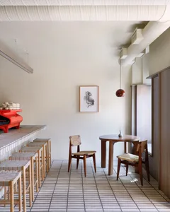 A warm and inviting kitchen space with wooden floors, white walls, a red dining table, and multiple chairs and benches
