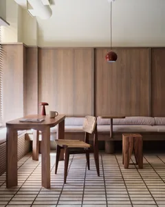 A well-lit living space with a dining table, chairs, couches, and a lamp, featuring wooden floors and walls