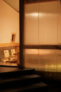 A modern living space with a glass wall separating two areas, featuring three wooden chairs and an open, minimalistic atmosphere