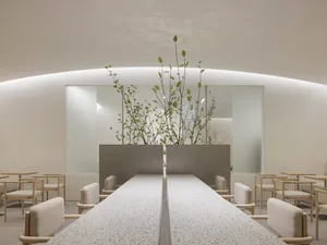 A clean and inviting restaurant interior with a long dining table, chairs, and potted plants