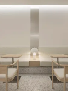 Empty minimalist room with white walls and floors, featuring three couches, two chairs, and a small lamp, creating a calm and minimalistic atmosphere