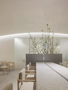 A modern restaurant dining area with multiple tables and chairs, adorned with potted plants and a clean, minimalistic ambiance