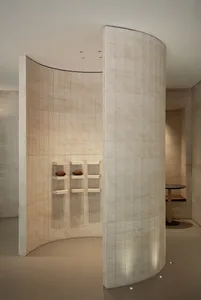 A clean and well-organized interior design showroom with a large white wall, wooden tables, and a bench, creating a bright and spacious atmosphere
