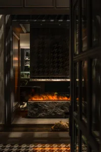 Warm and inviting living space with a stone and glass fireplace, surrounded by a black frame, and a rock wall, featuring two chairs and a dining table