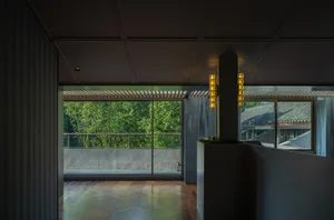 Open modern living area with white walls, wood flooring, and natural light from a large window overlooking trees, featuring potted plants and decorative vases