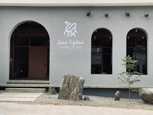 A modern building with a gray color scheme and a stone wall in front of a doorway, surrounded by two trees and a serene atmosphere
