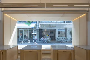 A bright and inviting space with a large window, chairs, dining tables, and an umbrella, suggesting a comfortable area for socializing or relaxation