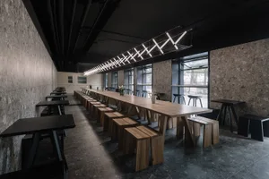 Empty restaurant with a long wooden dining table and chairs, surrounded by potted plants, creating an inviting and comfortable atmosphere