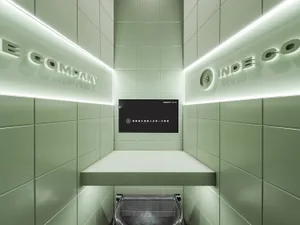 Bathroom with green tiles, two sinks, and a TV above one sink, in a well-lit space