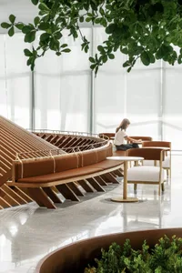 A calm and inviting indoor space with a large wooden bench and two smaller benches, featuring a woman sitting on one of them
