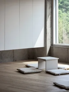 Cozy modern living area with a wooden floor, a white table, and pillows, well lit with clean lines and simple design elements