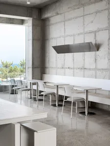 A modern restaurant interior with multiple dining tables and chairs, concrete walls, and a focus on functionality and clean lines