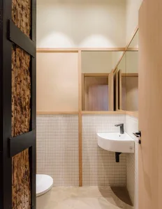 Modern bathroom with two white sinks, a mirror, and a wooden door, set against a tiled background