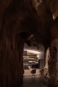 A cave bar with a circular bar surrounded by bottles, chairs, and natural cave walls, with modern amenities and inviting lighting