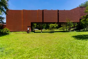 A relaxed outdoor space with a metal structure in the background, benches scattered throughout, and lush greenery adding to the ambiance