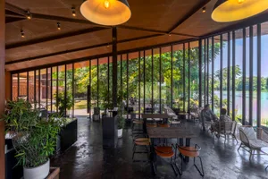 Dining area with chairs, cushions, potted plants, and a large window allowing natural light to enter