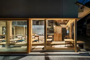 Open living area with wooden floors and walls, multiple chairs, a dining table, and a potted plant, well-lit and inviting